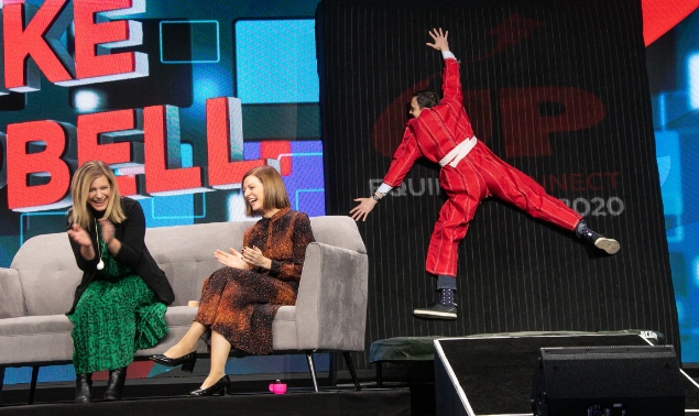 two women sitting on a sofa laughing at a man