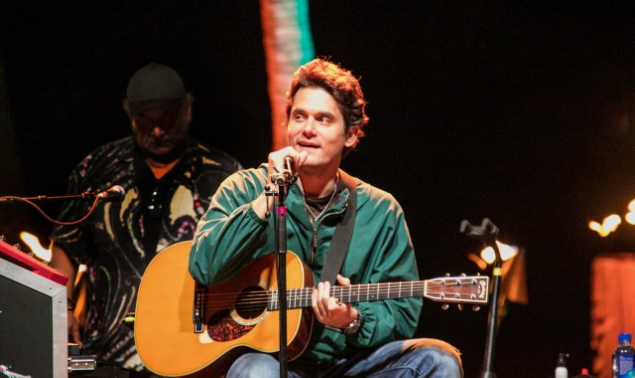 A man wearing green jacket playing a guitar and about to sing
