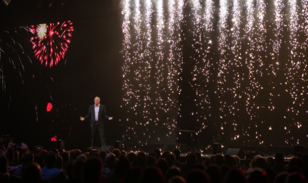 A man at the stage with fireworks background on screen