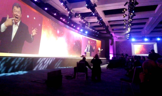 A side shot image of a stage with a man speaking in an event